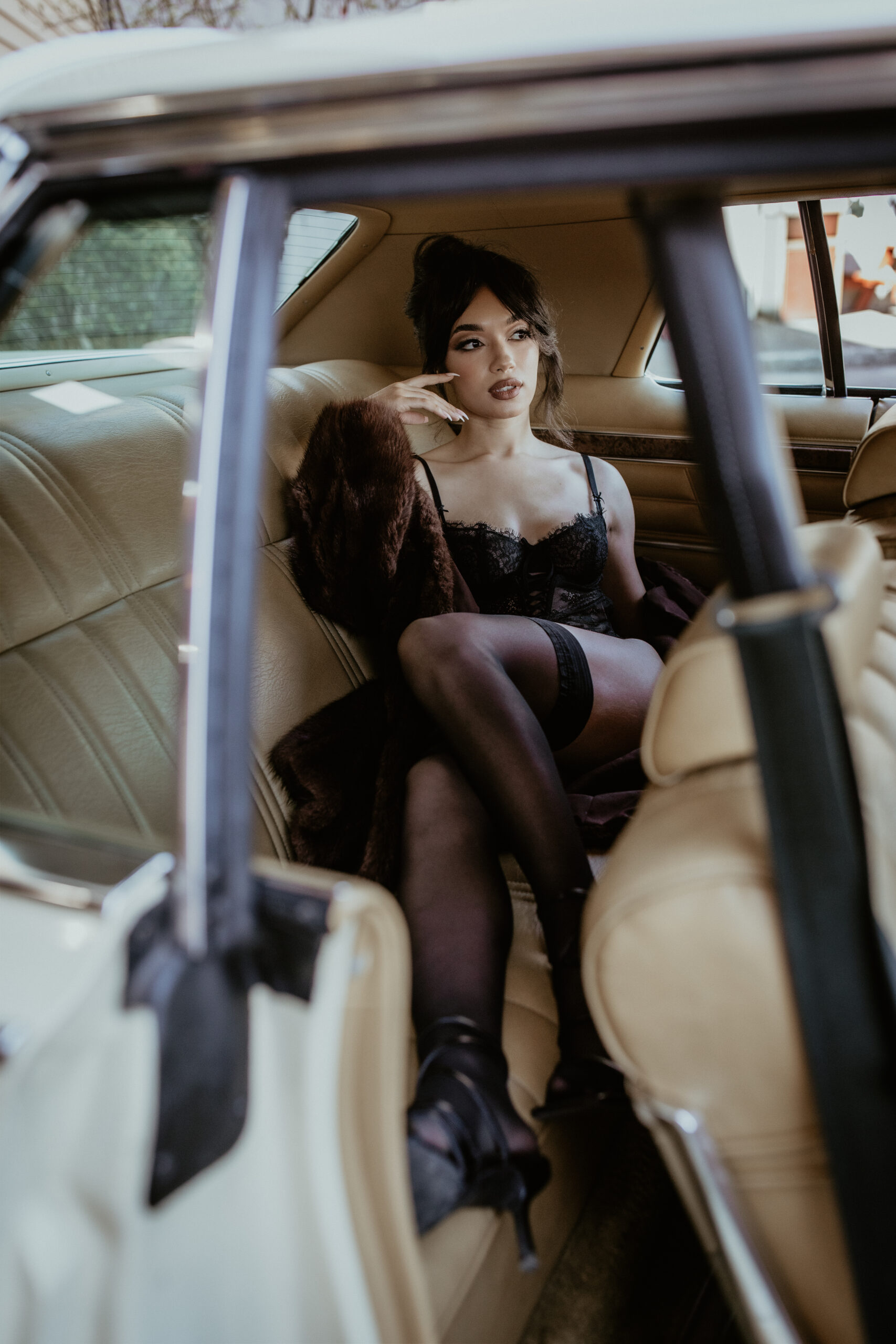Elegant woman in black lace boudoir set and fur coat, posing confidently in a classic car in Portland, Oregon, showcasing beauty and sophistication.